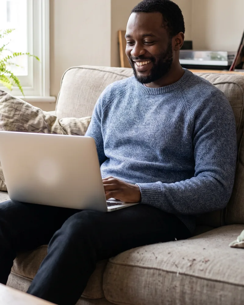 A smiling man on his sofa using a laptop